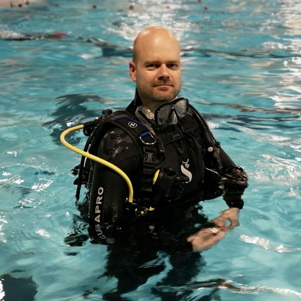 Arno Meijs gekleed in een duikpak met volledige duikuitrusting op zijn rug, staand in zwembadwater